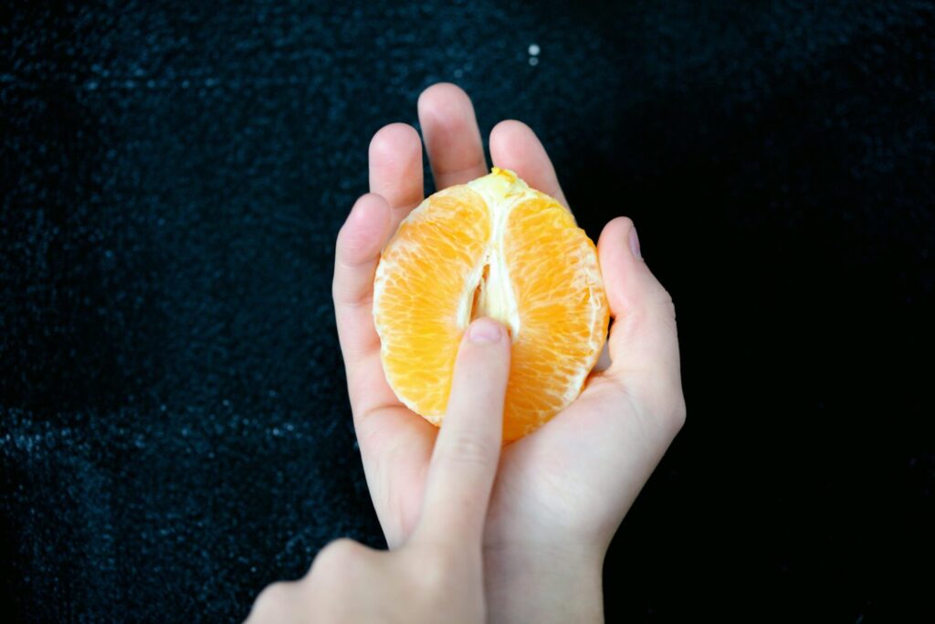 Bild einer halbierten Orange auf deren Fruchtknoten mit einem Finger gedeutet wird