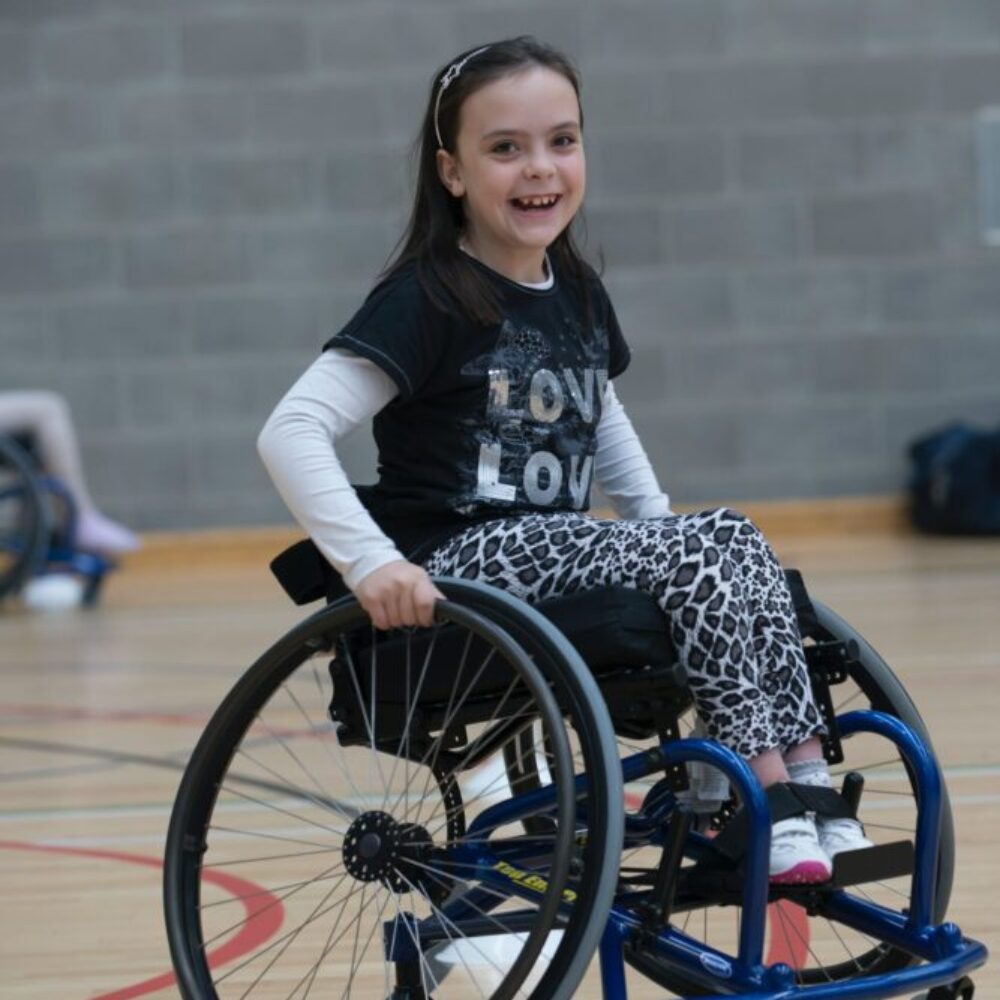 Ein im Rollstuhl sitzendes Kind lacht beim Sport